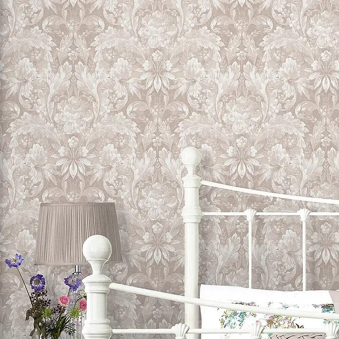 Laura Ashley Vliestapete Vliestapete Apolline - Grau, Floral, 10 x 0,52 m - Beigefarbene Tapete mit hellem, opulentem Blumenmuster, an einer Schlafzimmerwand hinter einem weißen Bett und einer Lampe.