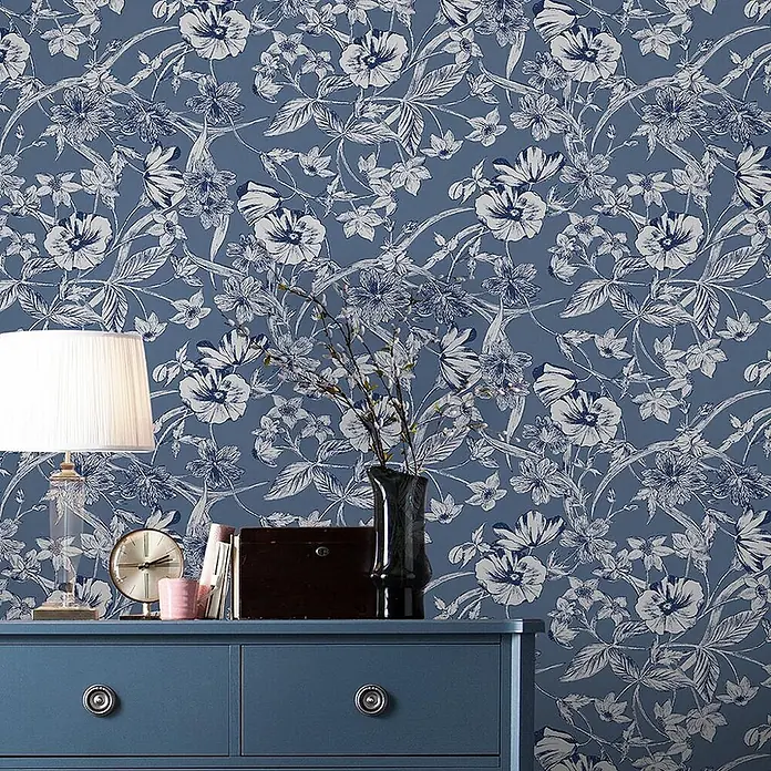 Laura Ashley Vliestapete Sommerhügel - Blau, Floral, 1.000 x 52 cm - Blautapete mit weißem Blumenmuster, an einer Wand über einer blauen Kommode.