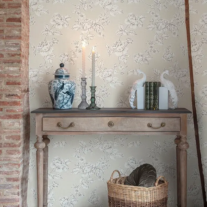 Laura Ashley Vliestapete Pollington Rosen - Naturbelassen, Floral, 1.000 x 52 cm - Rustikale Holzkonsole mit dunkler Platte, dekoriert mit blauer Vase, Kerzen und Büchern, in einem Raum mit Blumentapete.