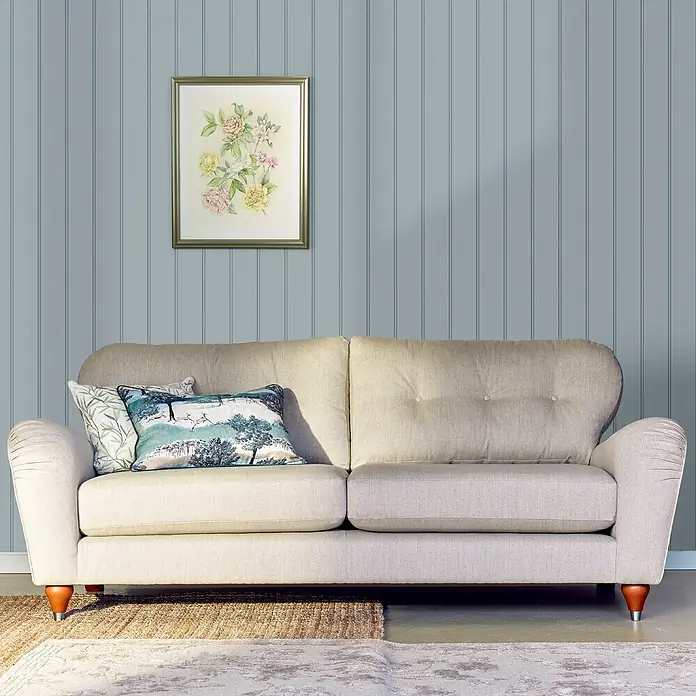 Laura Ashley Vliestapete Vliestapete Holzvertäfelung - Blau, Streifen, 10 x 0,52 m - Ein hellbeiges Stoffsofa mit zwei gemusterten Kissen vor einer blauen Paneelwand im Wohnzimmer.