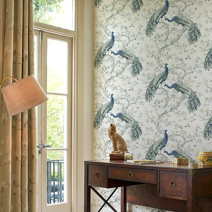Laura Ashley Vliestapete Vliestapete Belvedere Pfau - Blau/Weiß, Floral - Tapete mit Pfauenmuster in Blau und Weiß an einer Wand, passend zu einem dunklen Holzschreibtisch.
