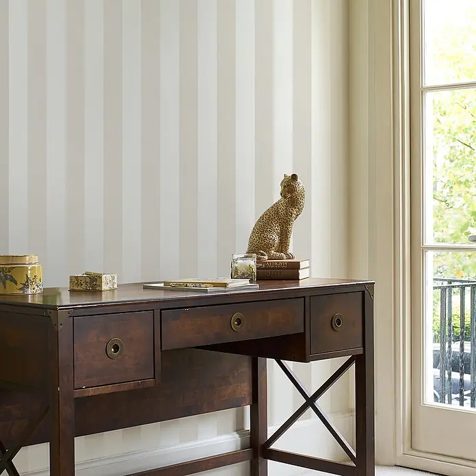 Laura Ashley Vliestapete Vliestapete Perlmuttstreifen - Leinen, Ornament - Dunkler Holzschreibtisch mit Messingbeschlägen und Kreuzstrebenbeinen, als Konsolentisch mit Dekoartikeln inszeniert.