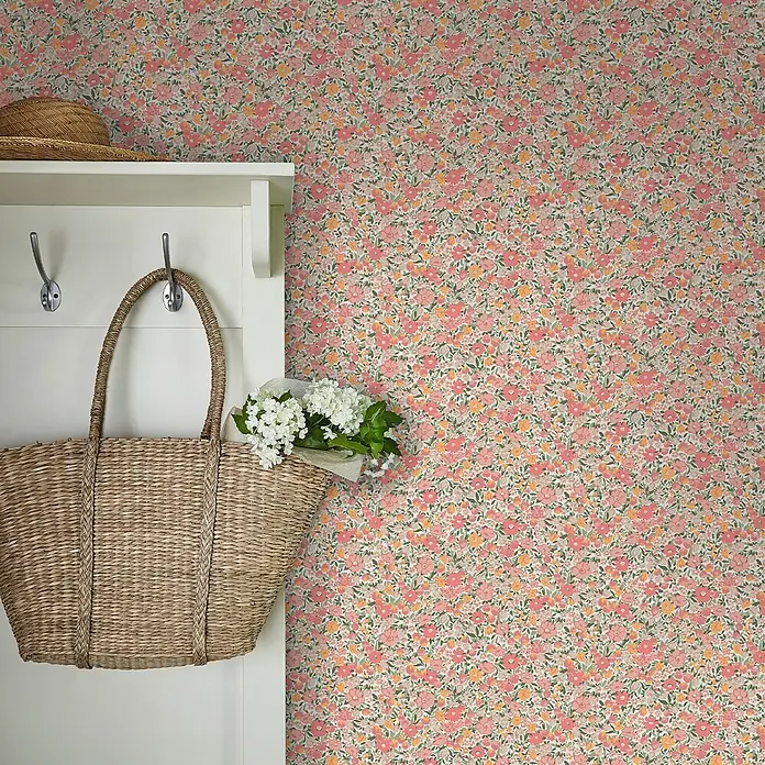 Laura Ashley Vliestapete Vliestapete Loveston Chrysanthemen - Rosa, Floral, 10 x 0,52 m - Florale Tapete in Pink, Orange und Grün, schmückt eine Wand neben einer weißen Garderobe mit Strohhut und Korb.