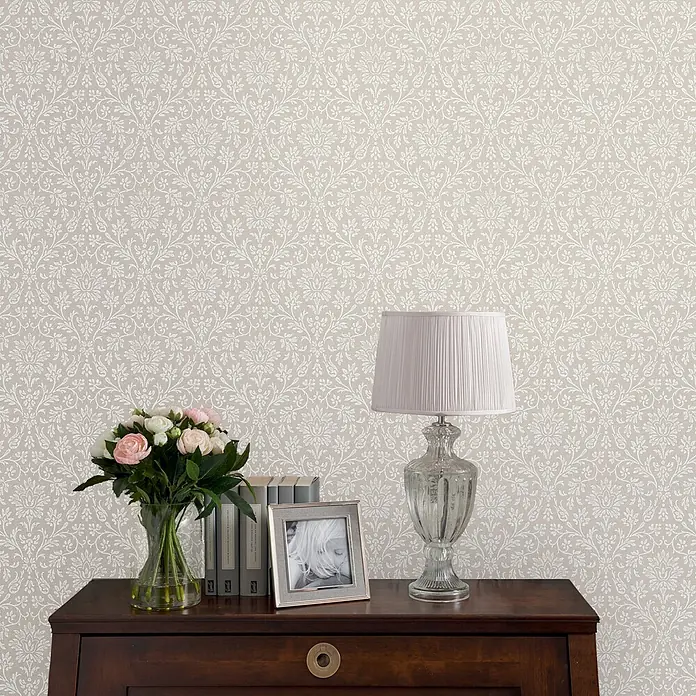 Laura Ashley Vliestapete Annecy - Hellgrau, Ornament, 1.000 x 52 cm - Beige Tapete mit weißem Blumen-Damastmuster an einer Wand.