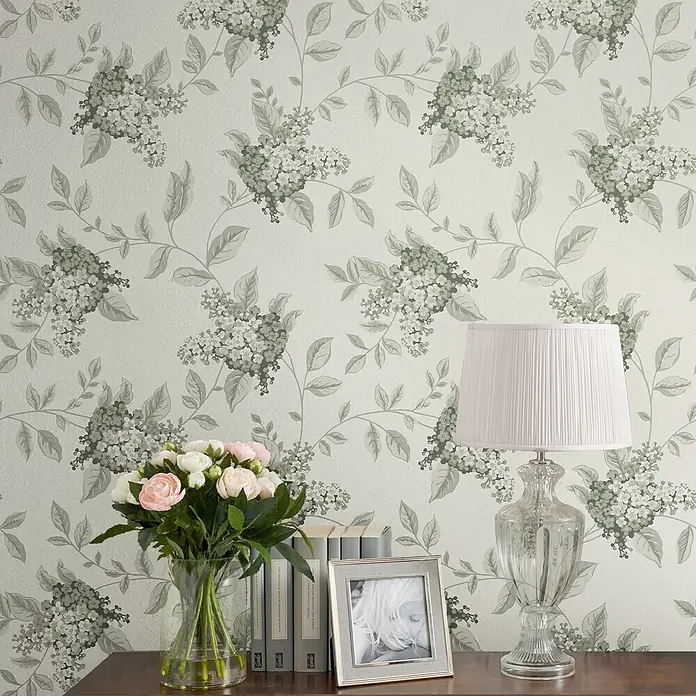 Laura Ashley Vliestapete Vliestapete Portland - Grün, Ornament, 10 x 0,52 m - Florale Tapete mit grünen Blättern und weißen Blüten, ziert eine Wand über einem Holztisch.