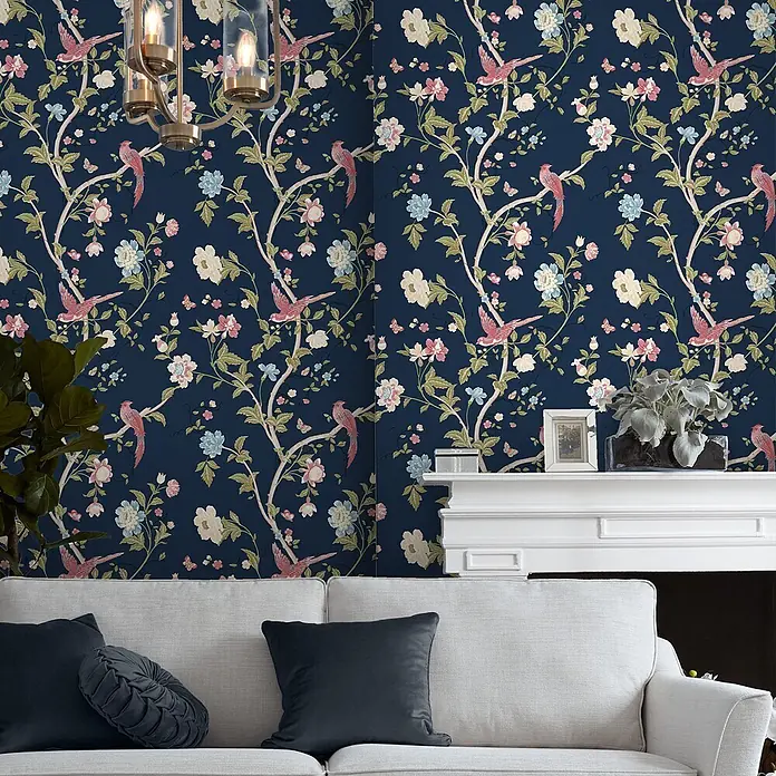 Laura Ashley Vliestapete Sommerpalast - Blau, Floral, 1.000 x 52 cm - Dunkelblaue Blumen- und Vogel Tapete in einem Wohnzimmer über einem weißen Sofa und Kamin.