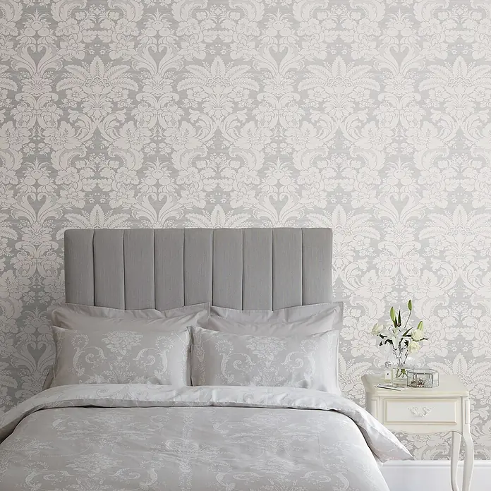Laura Ashley Vliestapete Martigues Damast - Grau/Weiß, Floral, 1.000 x 52 cm - Graues gepolstertes Kopfteil und gemusterte Bettwäsche mit passender Tapete in einem Schlafzimmer.