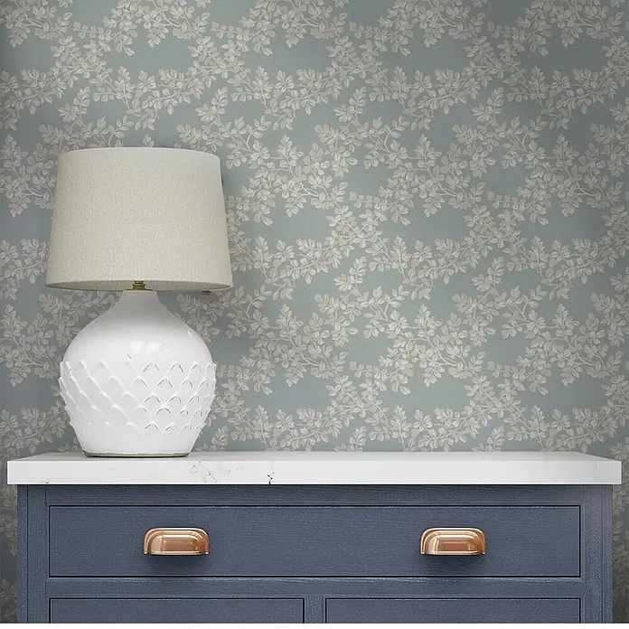 Laura Ashley Vliestapete Burnham - Hellblau, Floral, 1.000 x 52 cm - Sanfte blau-graue Tapete mit hellem beigem Blattmuster, in einer Raumumgebung präsentiert.
