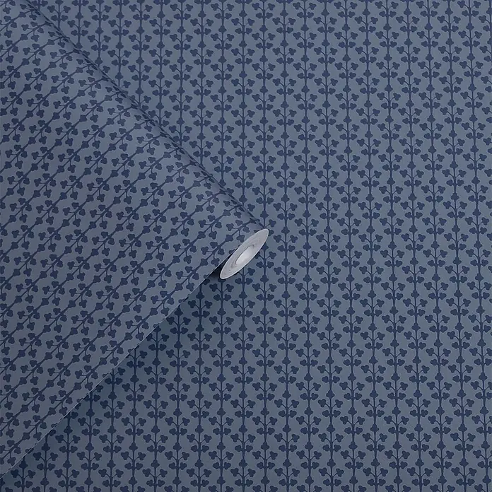 Laura Ashley Vliestapete Seaham - Blau, Grafisch, 1.000 x 52 cm - Blaue Tapete mit sich wiederholendem Muster aus dunkelblauen herzförmigen Blättern an vertikalen Ranken, teilweise ausgerollt.
