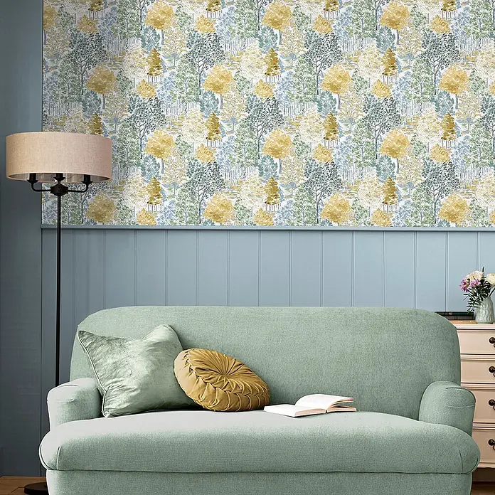 Laura Ashley Vliestapete Bernwood - Gelb, Floral, 1.000 x 52 cm - Waldmotiv-Tapete mit grünen, gelben und blauen Bäumen auf weißem Grund, schmückt eine Wohnzimmerwand über hellblauer Wandvertäfelung.