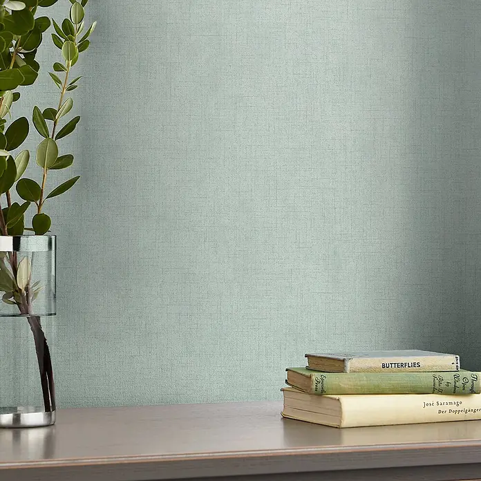 Laura Ashley Vliestapete Vliestapete Einfarbig - Blau, Uni, 10 x 0,52 m - Hellgrüne Tapete mit feiner Webstruktur an einer Wand, dekoriert mit Pflanze und Büchern.