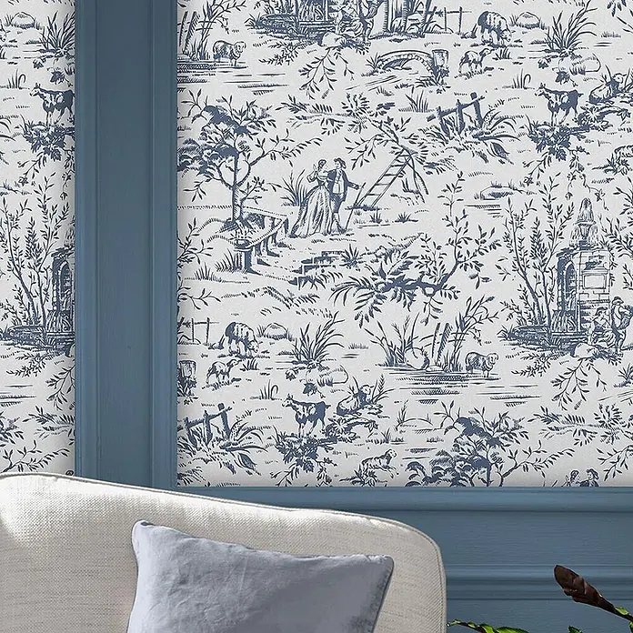 Laura Ashley Vliestapete Toile de Jouy - Blau, Floral, 1.000 x 52 cm - Blau-weiße Toile de Jouy Tapete mit pastoralen Szenen an einer Wand, gerahmt von blauer Wandvertäfelung, mit Sessel im Vordergrund.