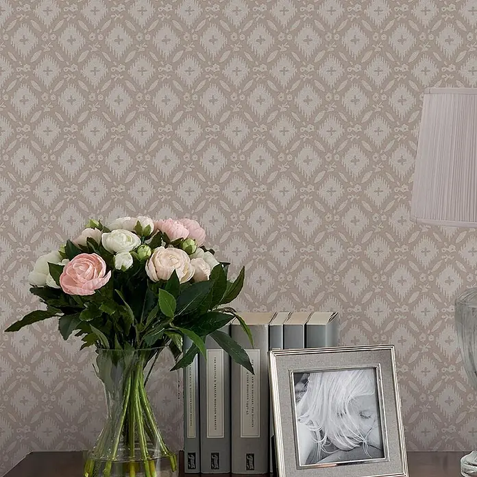 Laura Ashley Vliestapete Whitebrook - Grau, Ornament, 1.000 x 52 cm - Beige Tapete mit hellem geometrischem Rauten- und Kreuzmuster, hinter einem Tisch mit Blumen und Büchern.