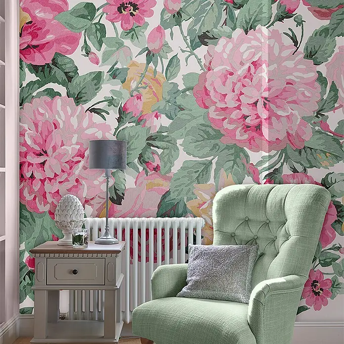 Laura Ashley Fototapete - Vlies - Lebhafte pink-grüne Blumentapete bedeckt eine Wand in einem Raum, hinter einem grünen Sessel und Beistelltisch.