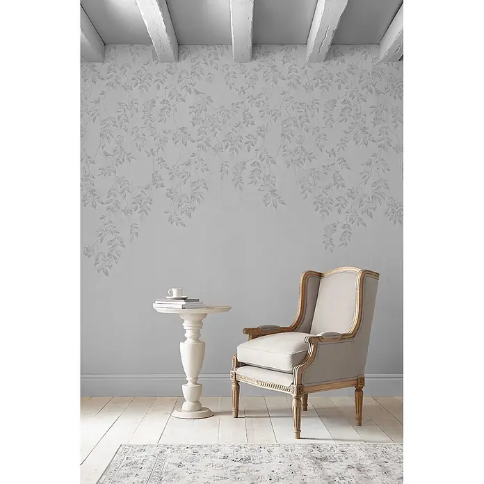 Laura Ashley Fototapete - Vlies - Hellgraue Tapete mit zartem Blumen- und Vogelmuster, die einen gemütlichen Raum mit Sessel und Beistelltisch schmückt.