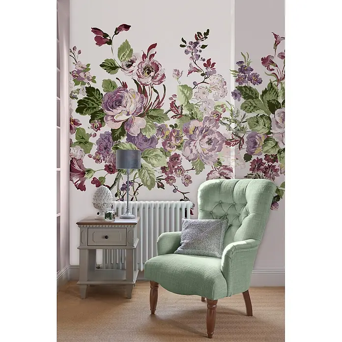 Laura Ashley Fototapete - Vlies - Ein hellgrüner Polstersessel mit geknöpfter Rückenlehne und Holzbeinen steht neben einem Beistelltisch in einem Raum mit Blumentapete.