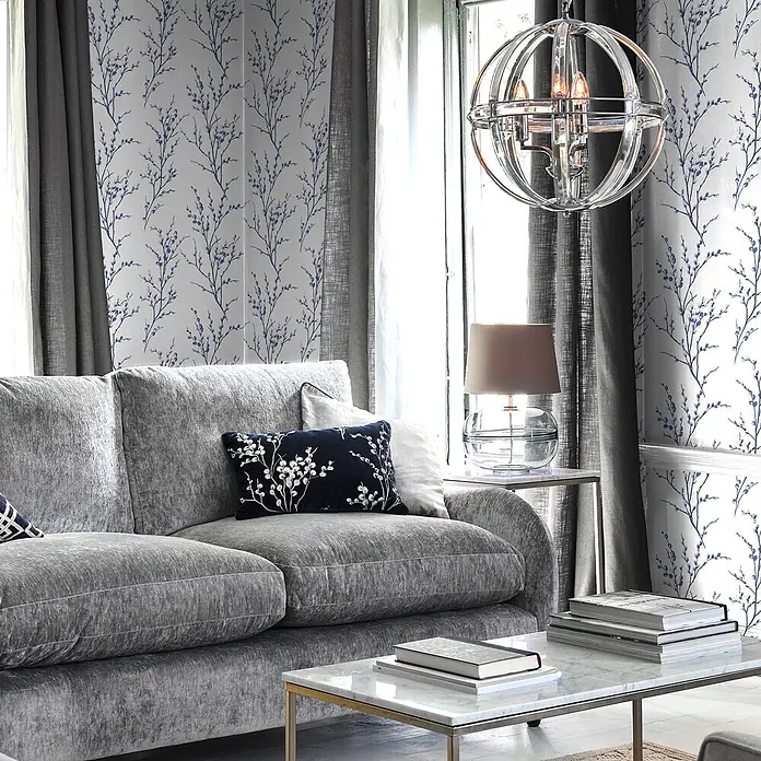 Laura Ashley Vliestapete Vliestapete Weidenkätzchen - Dunkelblau/Weiß, Floral, 10 x 0,52 m - Modernes Wohnzimmer mit einem plüschigen grauen Sofa, Marmor-Couchtisch und heller Tapete mit blauen Blumenmustern.