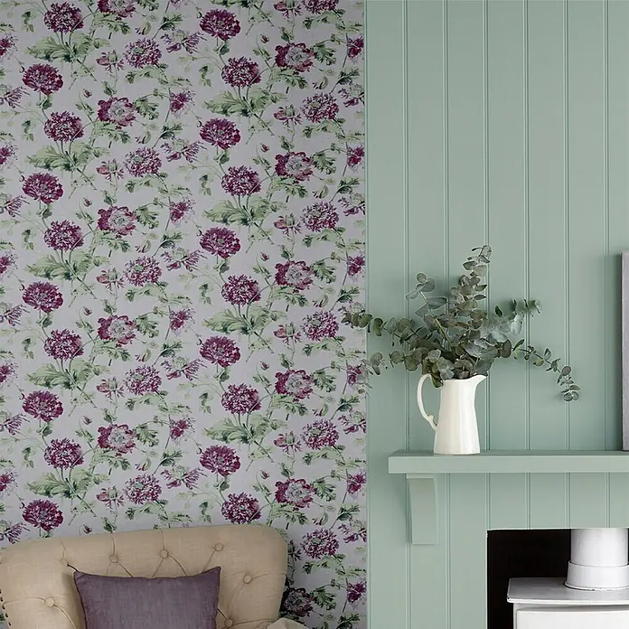 Laura Ashley Vliestapete Vliestapete Hepworth - Lila, Floral, 10 x 0,52 m - Florale Tapete mit lila und grünen Blüten, die eine Wand in einem Raum mit hellgrüner Vertäfelung und einem getufteten Sesselteil schmückt.
