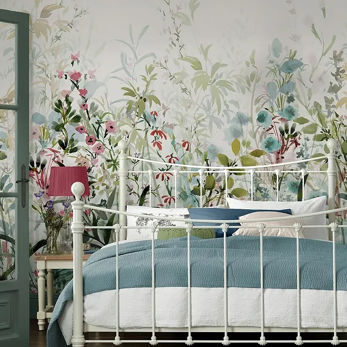 Laura Ashley Fototapete - Vlies - Ein weißes Metallbett mit einer türkisfarbenen Decke in einem Schlafzimmer mit Blumenmustertapete.