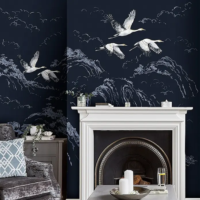 Laura Ashley Fototapete - Vlies - Dunkelblaue Tapete mit weißen Kranichen, Bergen und Wolken, schmückt eine Wohnzimmerwand über einem Kamin.