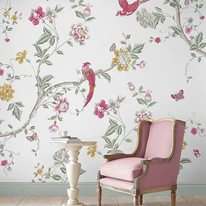 Laura Ashley Fototapete - Vlies - Elegante Chinoiserie-Tapete mit rosa und gelben Blüten und roten Vögeln schmückt eine Wand in einem raffinierten Raum.