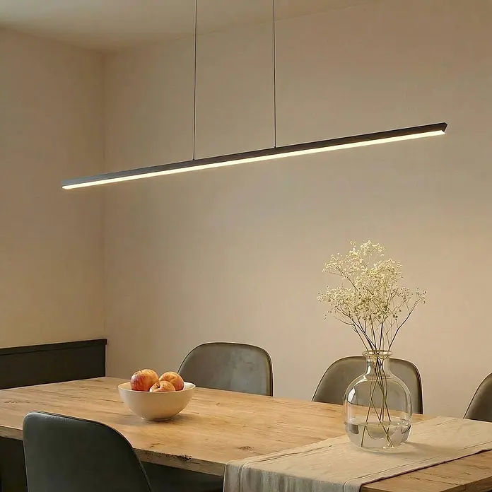 Lucande Pendelleuchte Solvar - schwarz, Schwarz - Dunkle lineare LED-Pendelleuchte über einem Esstisch mit Stühlen, Obstschale und Blumenvase.