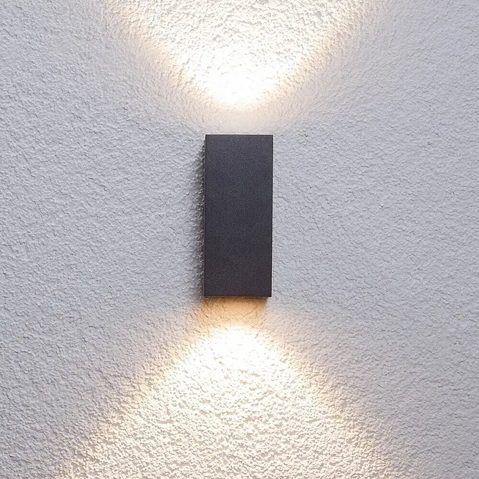 Lucande Außenwandleuchte Tavi - schwarz, schwarz, IP54 - Dunkelgraue, rechteckige Wandleuchte, die eine strukturierte Wand mit warmem Licht nach oben und unten beleuchtet.