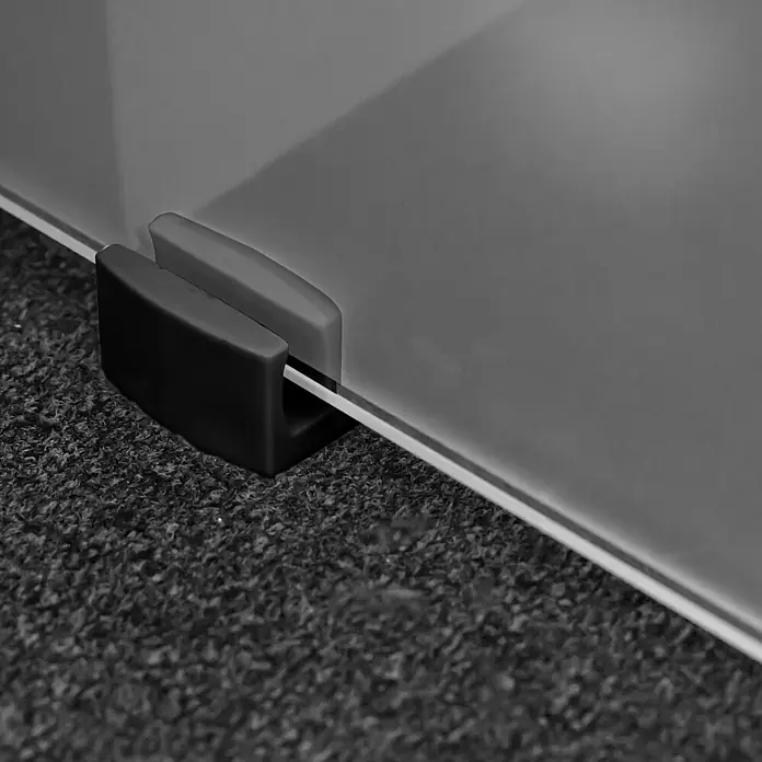 Inova Schiebetür-Komplettset Glas vollsatiniert mit Stabgriff in schwarz - 900 x 2.035 mm - Dunkel- und hellgraue Kunststoffklemme, die eine klare Glasplatte sicher hält und ihre stabilisierende Funktion demonstriert.