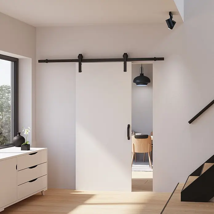Inova Schiebetür-Komplettset Holz Weiß mit Beschlag und Bügelgriff in schwarz -  - Moderne weiße Schiebetür im Scheunentor-Stil mit schwarzer Beschlag und Griff, leicht geöffnet zu einem Innenraum.