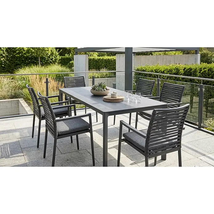 Acamp Gartenmöbel-Set New Jersey - 7 -tlg., Aluminium, Anthrazit - Moderne graue Outdoor-Essgruppe mit rechteckigem Tisch und sechs Stühlen mit geflochtenen Rückenlehnen und dunklen Polstern auf einer Steinterrasse.