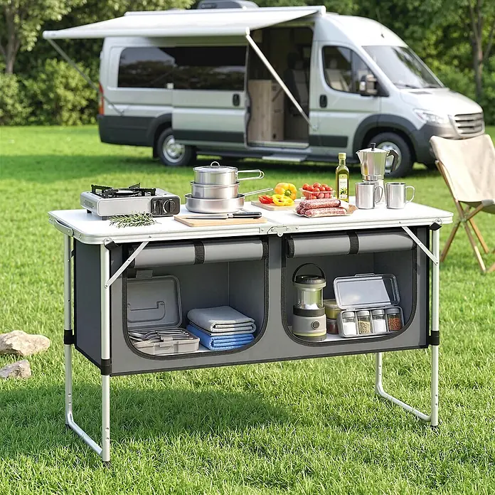 Outsunny Campingtisch - L x B x H: 120 x 47 x 70 cm, Aluminiumlegierung, Oxford, MDF, Silber, Klappbar - Tragbarer Campingküchenschrank mit weißer Platte, grauen Staufächern und Aluminiumbeinen, zum Kochen im Freien neben einem Wohnmobil.
