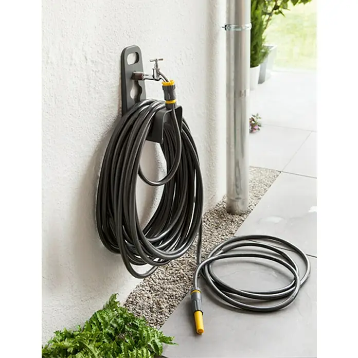 Neptun Wand-Schlauchhalterung - Kunststoff, Geeignet für: Handelsübliche Wasserhähne - Ein grauer Gartenschlauch hängt an einer grauen Halterung an einer weißen Wand. Der Schlauch ist aufgerollt und einsatzbereit.