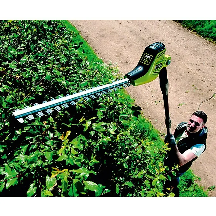 Ryobi Teleskop-Heckenschere RPT4545E - 450 W - Eine Ryobi 450W Heckenschere im Einsatz, um eine Hecke zu schneiden, mit einem Mann, der sie bedient. Das Gerät ist grün und schwarz.