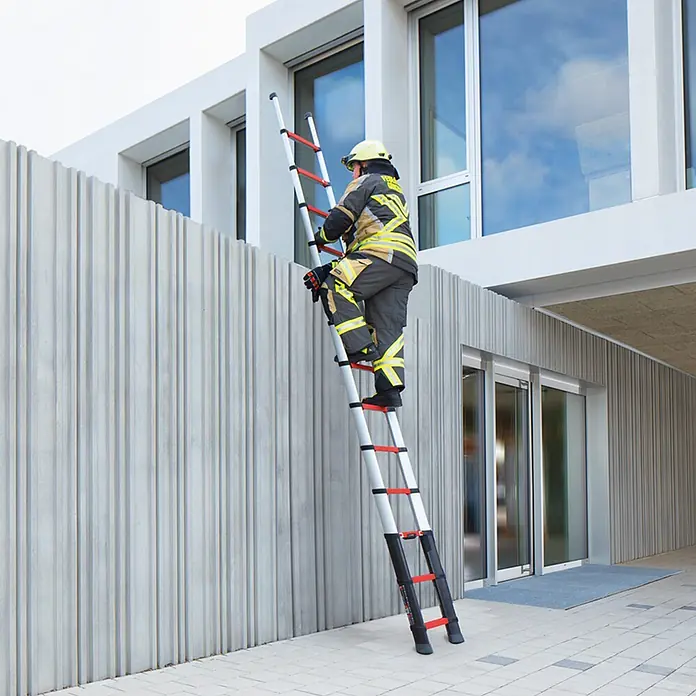 Telesteps Teleskopleiter Rescue Line Feuerwehr- & Rettungsleiter 4,1m – Teleskopleiter für 3 Pers - Anzahl Tritte: 13 Stk., Arbeitshöhe: 5.000 m, Belastbarkeit: 500 kg, Aluminium - Feuerwehrmann steigt eine ausgefahrene silberne, schwarze und rote Teleskopleiter an einem Gebäude hoch.