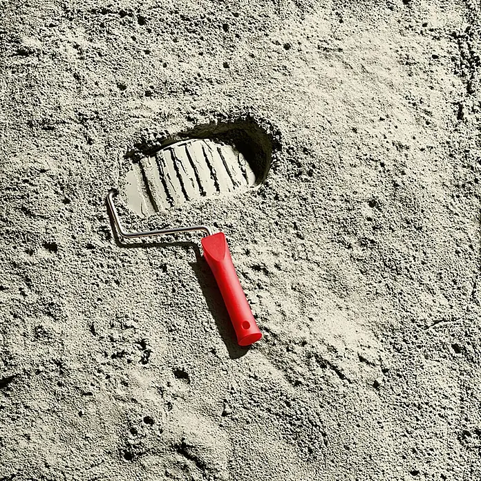 SCHÖNER WOHNEN-Farbe Wandfarbe Trendfarbe - Moon, Matt, 1 l, Konservierungsmittelfrei - Nahaufnahme eines roten Farbrollers in sandigem Gelände mit Fußabdruck.