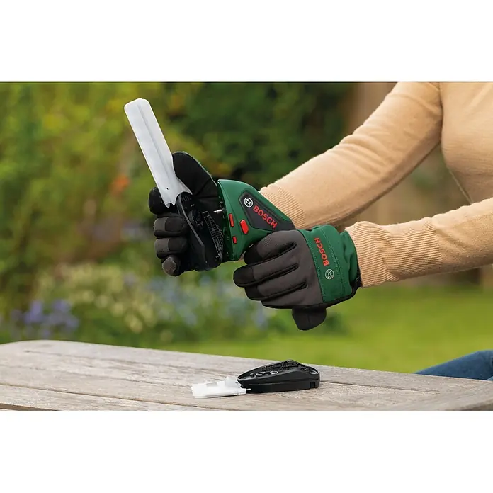 Bosch Akku-Gras- & Strauchschere ISIO 4 - 4 V, 1 Akku - Person in Bosch-Handschuhen montiert ein grünes, schwarzes Bosch-Gartengerät mit weißer Klinge.