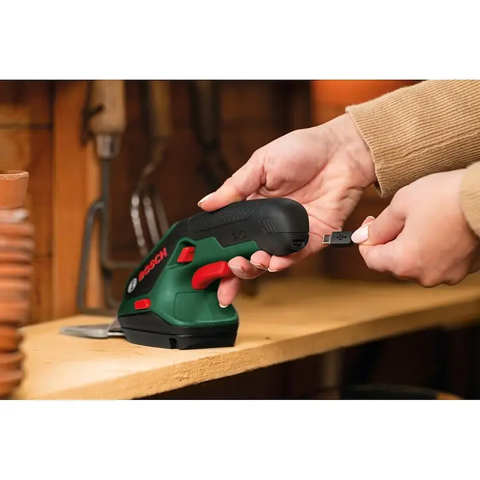 Bosch Akku-Gras- & Strauchschere ISIO 4 - 4 V, 1 Akku - Eine Person steckt ein USB-Kabel in ein grün-schwarzes Bosch Handgartenwerkzeug.