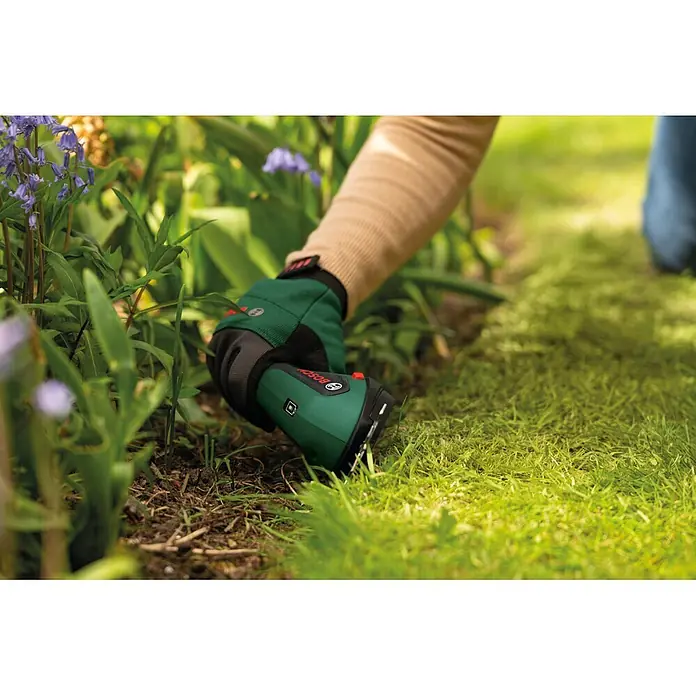 Bosch Akku-Grasschere ISIO 4 - 4 V, 1 Akku - Grün-schwarzer Bosch Grastrimmer in behandschuhter Hand, trimmt Rasen an einem Beetrand.