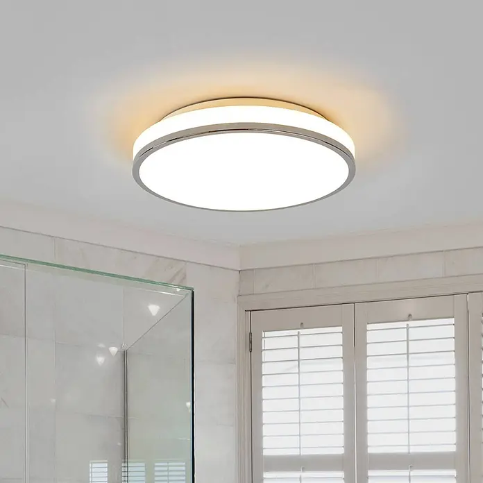 Lindby Deckenleuchte Lyss - weiß / opal - Runde LED-Deckenleuchte mit Chromrahmen und weißem Diffusor, die eine Badezimmerdecke warm beleuchtet.