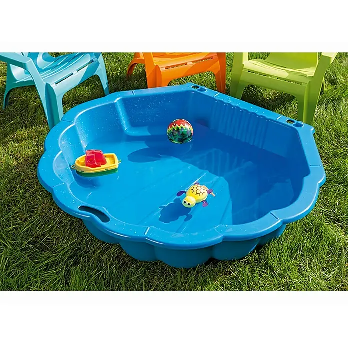 Wasser- & Sandmuschel Sandy - 88 x 102 x 21 cm, Blau - Blaues Planschbecken mit Spielzeug auf einer grünen Wiese, umgeben von farbigen Kinderstühlen.