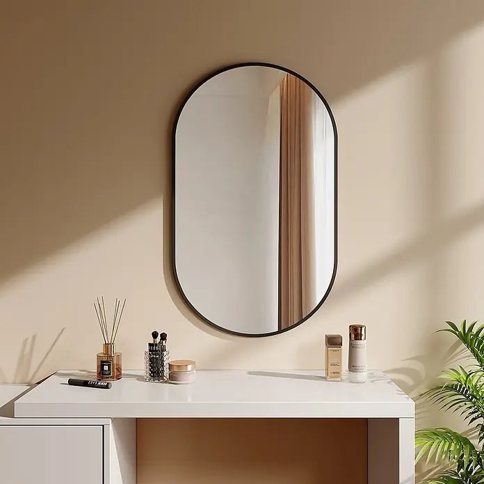 Emke Rahmenspiegel OM18 - 100 x 60 cm, Glas - Ein ovaler Spiegel mit schwarzem Rahmen über einem weißen Schminktisch mit Kosmetika und einem Diffusor vor beiger Wand.