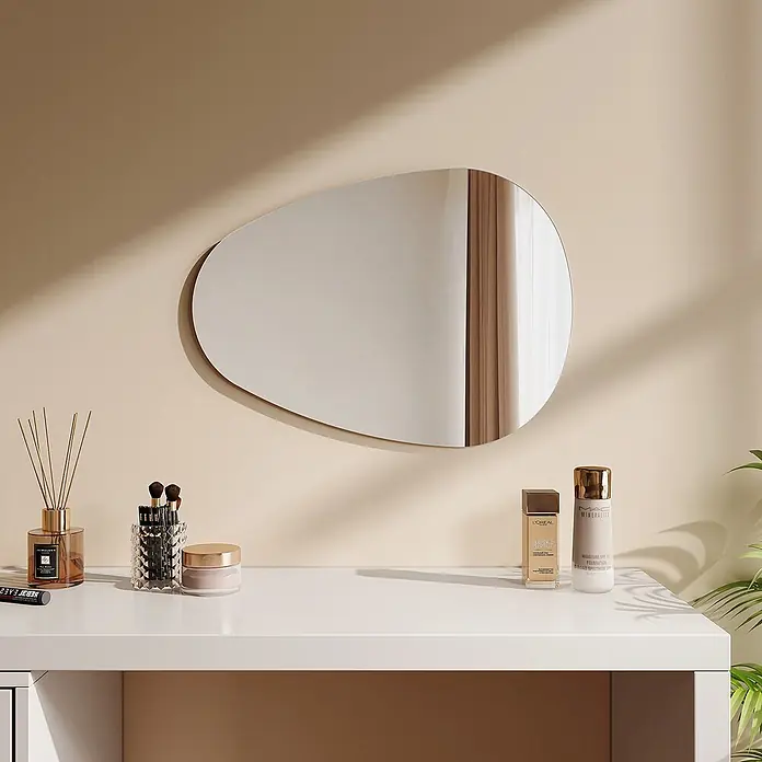 Emke Wandspiegel M33 - 60 x 45 cm - Organisch geformter Wandspiegel, der einen beigefarbenen Vorhang reflektiert, über einem weißen Schminktisch mit Beauty-Produkten.