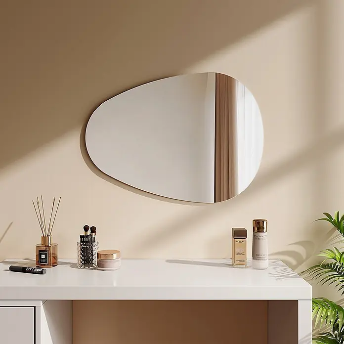 Emke Wandspiegel M33 -  - Ein unregelmäßig geformter Spiegel hängt über einem weißen Schminktisch und reflektiert ein Fenster. Kosmetikprodukte und eine Pflanze stehen auf dem Tisch.