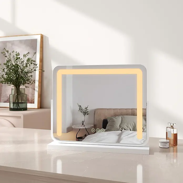 Emke Kosmetikspiegel CM08 - Rechteckig, Weiß - Weißer beleuchteter Schminkspiegel mit warmer LED-Lichtleiste, auf einem hellen Schminktisch stehend, ein Schlafzimmer reflektierend.