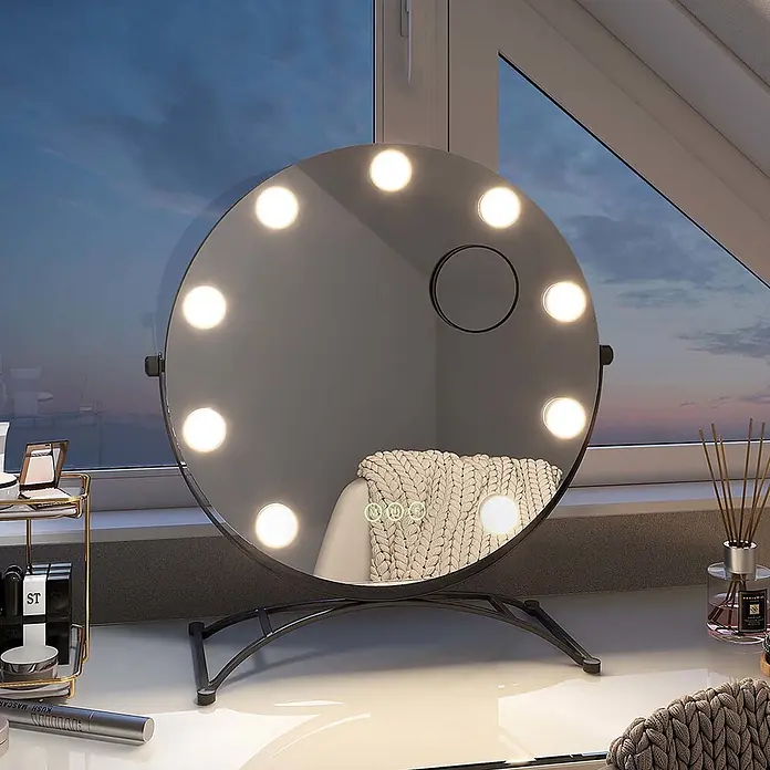 Emke Kosmetikspiegel CM11 - Rund, Schwarz - Runder LED-Schminkspiegel mit Lichtern und kleinem Vergrößerungsspiegel, auf dunklem Metallfuß, auf einem Schreibtisch.