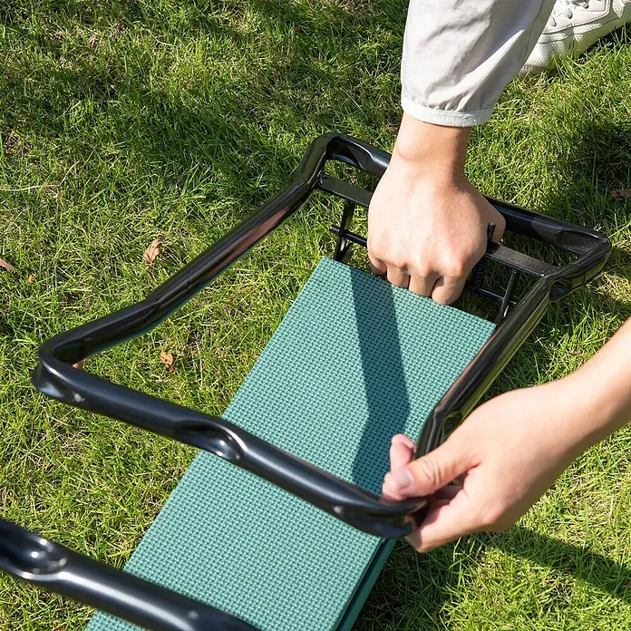 Outsunny Kniebank Schwarz+Dunkelgrün 58L x 28B x 49H cm -  - Person stellt einen schwarzen Gartenhocker mit grüner Polsterung ein.