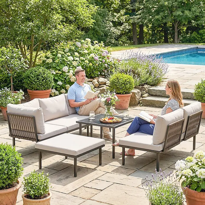 Outsunny Loungemöbel-Set - 6 -tlg., Metall, Polyester, Schaumstoff, PP-Baumwolle, Verstellbare Füße, Hellgrau - Eine Outdoor-Sitzgruppe mit dunklen Rahmen, geflochtenen Details und hellbeigen Kissen. Ein Paar entspannt auf Sofa und Sessel am Couchtisch.