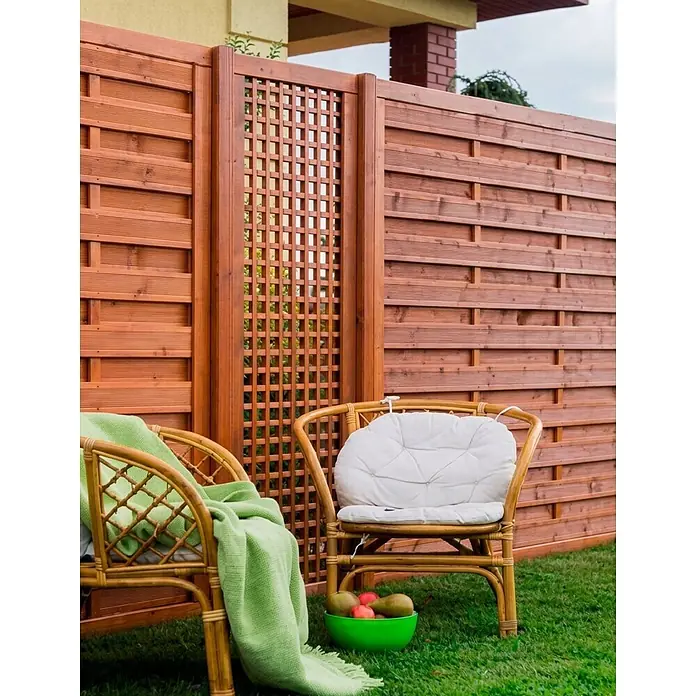 Werth Holz Rankgitter Lausanna - 59 x 179 cm, Holz, Bankiraibraun - Zwei natürliche Rattan-Sessel mit Kissen und grüner Decke vor einem Holzzaun für Entspannung im Freien.