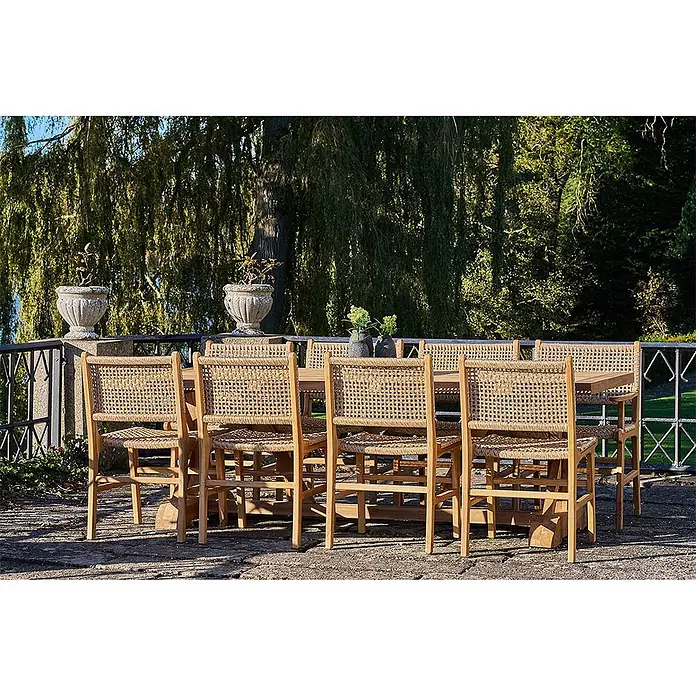 Ebuy24 Gartenstuhl Derby 2er-Set - 2 Stk., Massiv Teakholz, PE Rattan, Natur, B x T x H: 50 x 54 x 85 cm - Outdoor-Essgruppe: Holztisch und mehrere Stühle mit geflochtenen Rattansitzen und -lehnen auf einer Terrasse.