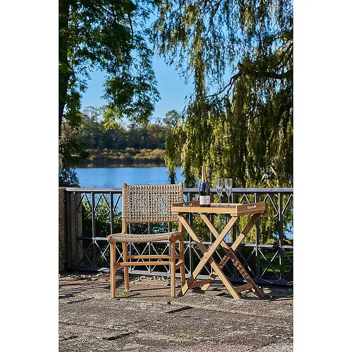 Ebuy24 Gartenstuhl Derby 2er-Set - 2 Stk., Massiv Teakholz, PE Rattan, Natur, B x T x H: 50 x 54 x 85 cm - Outdoor-Stuhl aus Holz mit geflochtener Rückenlehne und Sitzfläche und passendem Klapptisch mit Tablett auf einem Balkon.
